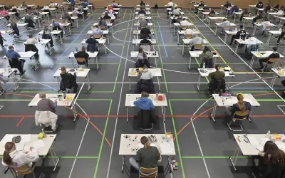 Viele Schüler sitzen in einer Sporthalle an Tischen, um zum Abitur zu schreiben.