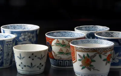 Vielfalt der japanischen Porzellankunst: Mehrere kleine Becher mit traditionellen Mustern, darunter Blumen und geometrische Formen, auf dunklem Hintergrund.