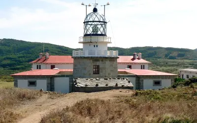 El faro de estaca de bares se alza imponente sobre la costa, con sus edificios blancos y tejados rojos rodeados de vegetación.