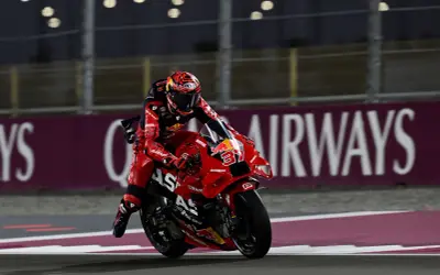 Piloto de MotoGP con traje rojo y casco a juego, en plena carrera. Busca sumar puntos en la clasificación.