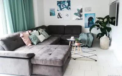 Gemütliches wohnzimmer einrichten mit einer großen, dunklen Couch, vielen Kissen in Pastelltönen und mintgrünen Akzenten. Bilder und eine Pflanze schmücken die Wand.