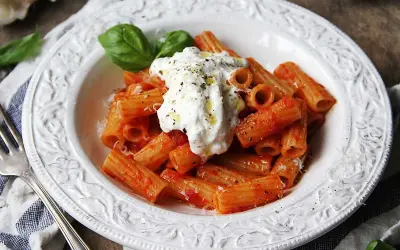 En krämig burrata pasta med rigatoni i tomatsås, toppad med färsk basilika och svartpeppar.