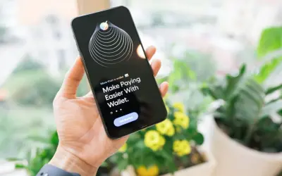 Dłoń trzyma iPhone'a z aplikacją Wallet, która ułatwia płatności dzięki technologii NFC.