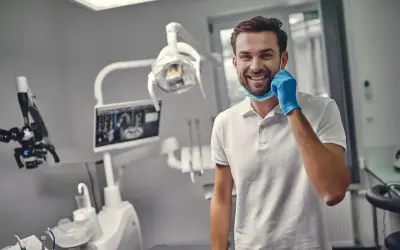 Uśmiechnięty dentysta w gabinecie, gotowy do pracy. Zastanawiasz się, ile trwa plombowanie zęba?