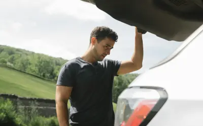 Mężczyzna zmartwiony przy otwartym bagażniku samochodu. W razie awarii pomoże ubezpieczenie assistance.