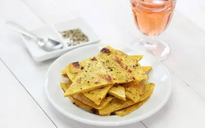 Une assiette de socca à la poêle, coupée en triangles et saupoudrée de poivre, à côté d'un verre de rosé.
