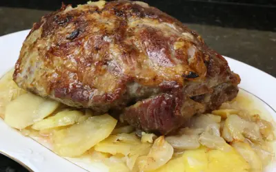 Cabezada de cerdo asada, jugosa y dorada, servida sobre patatas y cebolla caramelizada en un plato blanco.