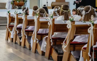 Dzieci w białych strojach i wiankach siedzą w kościele, czekając na uroczystość. Zastanawiasz się, ile trwa komunia?