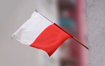 Flaga Polski powiewa na wietrze, biało-czerwona, ale w odwrotnej kolejności.