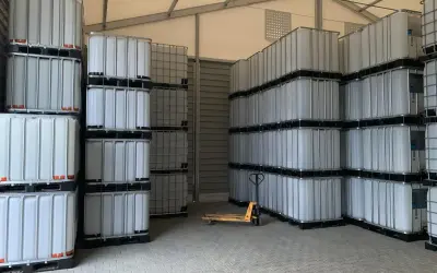 Magazyn pełen białych mauzerów 1000l, ułożonych w stosy. Widać wózek paletowy.