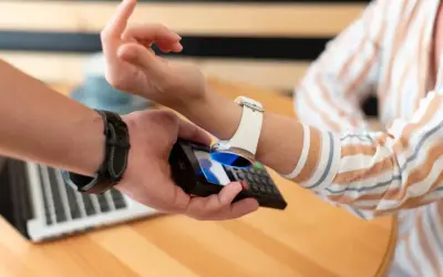 Zbliżenie na dłoń trzymającą telefon, który zbliża się do białego zegarka na ręce. Pokazuje, jak naładować zegarek telefonem.