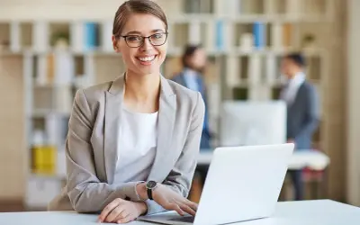 Lächelnde Frau mit Brille am Laptop, bereit für ihre medizinische Schreibkraft Ausbildung.
