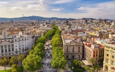 Słoneczna barcelona pogoda listopad. Ludzie spacerują aleją drzew, w tle widać miasto i góry.