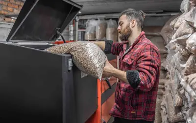 Mężczyzna w flanelowej koszuli wsypuje pellet do pieca. W tle worki z paliwem.