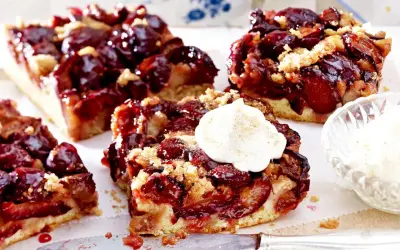 Saftige Pflaumenstücke auf einem lockeren Teig, bestreut mit Streuseln. Ein Stück gesunder Pflaumenkuchen mit einem Klecks Sahne.
