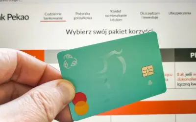 Dłoń trzyma zieloną kartę z logo Mastercard. Na ekranie komputera widać stronę banku Pekao, gdzie można dowiedzieć się, jak aktywować kartę Pekao przez internet.