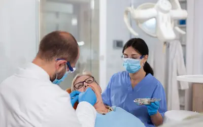 Dentysta zakłada białe plomby na NFZ starszej pacjentce. Asystentka stomatologiczna pomaga.