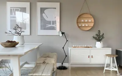 Ein Esszimmer im skandinavischen Stil mit einer warmen grau farbpalette. Ein weißer Tisch, eine Holzbank mit Schaffell und Kunstwerke an der Wand.