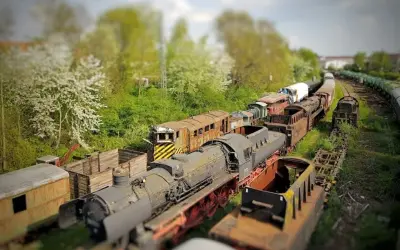 Un cementerio de trenes con efecto tilt shift, donde locomotoras y vagones oxidados parecen miniaturas bajo un cielo nublado.