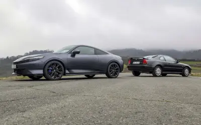 Due coupé Honda, una moderna e una classica, si incontrano su una strada di campagna. La nuova Honda Prelude 2026, grigio scuro, spicca accanto alla sua antenata.