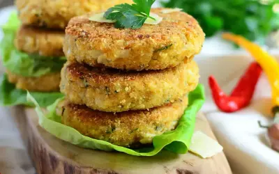 Złociste kotlety z kalafiora na 3 sposoby, podane na liściach sałaty, z parmezanem i natką pietruszki. Obok czerwone i żółte papryczki chili.