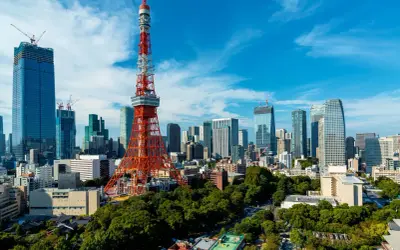 Tokio Tower góruje nad nowoczesnym miastem z wieżowcami w budowie i zielonymi drzewami.