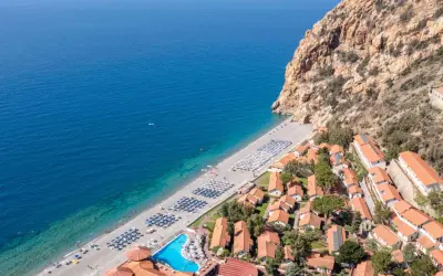 Villaggio turistico con spiaggia attrezzata e piscina, incastonato tra il mare blu e una scogliera rocciosa. Un luogo ideale per esplorare i paesi vicino Catania sul mare.