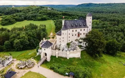 Zamek Bobolice, malowniczo położony na skale, otoczony zielenią i lasami.