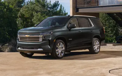 Ciemnozielony Chevrolet Tahoe High Country z chromowanymi felgami stoi przed nowoczesnym domem.