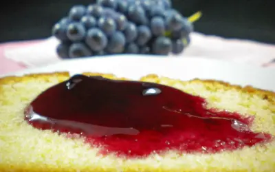 Tranche de gâteau moelleux nappée d'une généreuse gelée de raisin, avec une grappe de raisins bleus en arrière-plan.
