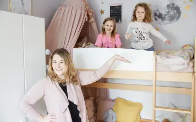 Uroczy mały pokój dla rodzeństwa w bloku. Dwie dziewczynki bawią się na łóżku piętrowym, a mama prezentuje przestrzeń.