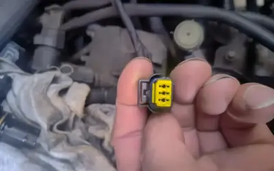 Wtyczka z żółtym wkładem, być może związana z błędem **dtc p1693 volkswagen**. W tle widać fragmenty silnika.
