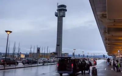 Wieża kontrolna na oslo lotnisko. Samochody czekają na pasażerów, a bagaże są wyładowywane.