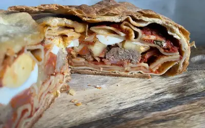 Fetta di timballo di pasta con strati di pasta, uova sode, ragù e carne, racchiuso in una crosta dorata.