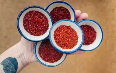Dłoń trzyma cztery małe miseczki z płatkami papryki do kimchi.