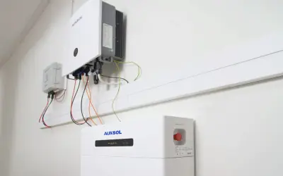 Nowoczesny bank energii do domu, zamontowany na ścianie, z widocznym falownikiem i modułem bateryjnym.