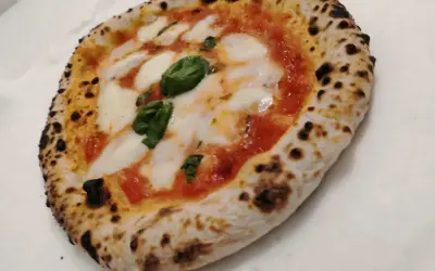 Une authentique pizza napolitaine, avec sa croûte gonflée et légèrement brûlée, garnie de sauce tomate, de mozzarella fondante et de feuilles de basilic frais.