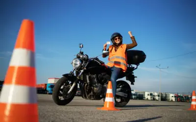 Szczęśliwa motocyklistka z prawem jazdy kategorii A3 w ręku, siedząca na motocyklu, świętuje sukces na placu manewrowym.