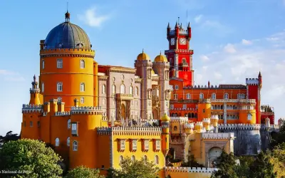Buntes Sintra Pena Palace mit gelben und roten Türmen, einer blauen Kuppel und einem Uhrenturm unter blauem Himmel.