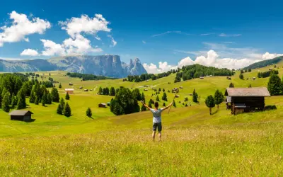 Ein Wanderer genießt die Aussicht auf eine Alm mit Berghütten und Wäldern. Perfekt für eine Mehrtageswanderung in den Dolomiten.
