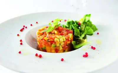 Délicieux tartare de truite aux agrumes, avocat et poivrons, garni de jeunes pousses et de baies roses sur une assiette blanche.