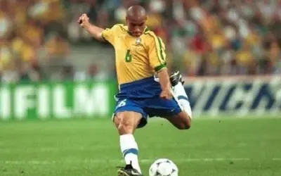 Roberto Carlos, z numerem 6 na koszulce, wykonuje potężne uderzenie piłki na boisku.