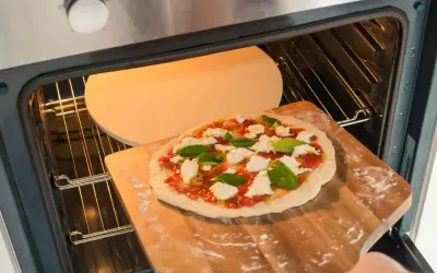 Przygotowania do dnia pizzy 2026: świeża pizza z mozzarellą i bazylią wsuwana na rozgrzany kamień w piekarniku.