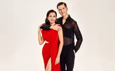 Para finaliści "Tańca z Gwiazdami" w eleganckich strojach: ona w czerwonej sukni, on w czarnej, prześwitującej koszuli.