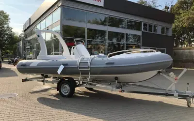 Szara łódź typu RIB na przyczepie przed budynkiem z logo Yamaha.