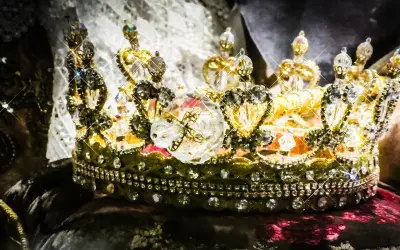 Korona zdobiona klejnotami, symbol bogactwa i władzy, przypomina o globalnym wydobyciu złota.