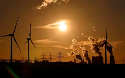 Silhouetten von Windrädern und rauchenden Industrieanlagen im Sonnenuntergang. Ein Bild, das zum Nachdenken über Stromkosten Norwegen vs. Deutschland anregt.