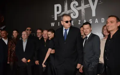 Grupa aktorów z filmu "Psy" pozuje do zdjęcia. W centrum mężczyzna w okularach przeciwsłonecznych i garniturze.