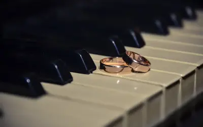 Dos alianzas de oro descansan sobre teclas de piano, evocando la pregunta: ¿cuanto pesa una alianza de oro?
