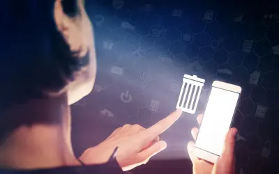 Dłoń dotyka ikony kosza na śmieci na ekranie smartfona, symbolizując czyszczenie telefonu i porządkowanie danych.